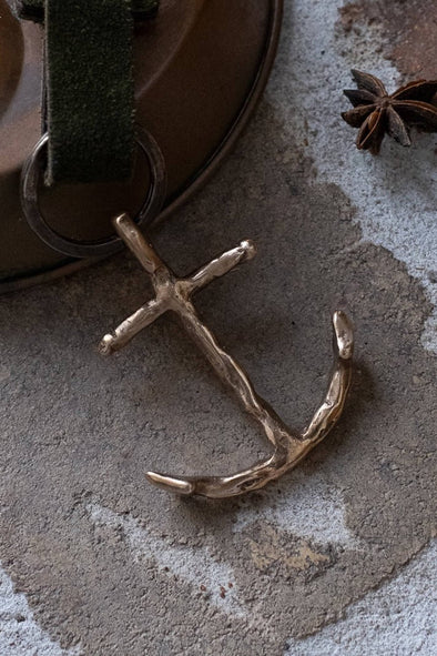 Bronze anchor pendant on a textured surface with star anise in the background