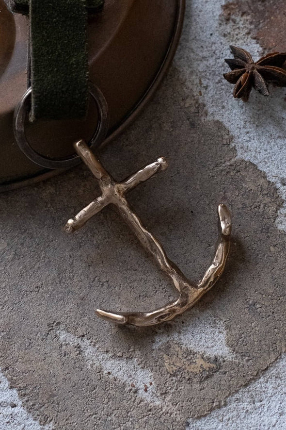 Bronze anchor pendant on a textured surface with star anise in the background